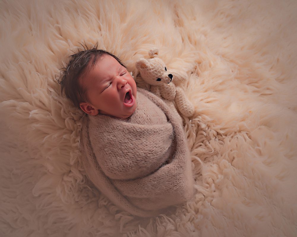 A swaddled newborn baby in a knitted blanket. Newborn photographs of a baby yawning. Manchester photography studio.