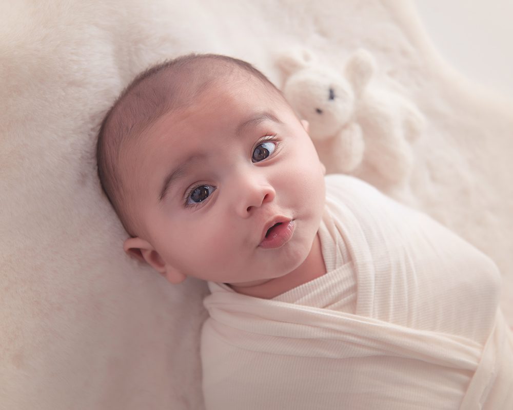 A swaddled newborn baby in a knitted blanket with a teddy bear. Professional photography of a newborn baby. Taken at our Manchester photography studio.